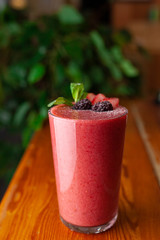 Red smoothie decorated with berries and mint on a table