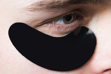 Skin care. Black pearl extract. Minimizes puffiness and reduce dark circles. Eye patches for men. Man with black eye patches close up. Metrosexual concept. Focused treatments for under eye area