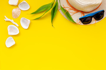 Planning vacation to the seaside with straw hat, sun glasses, shells on yellow background top view space for text