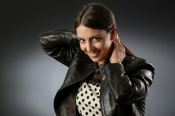 Studio portrait of a cute smiley woman wearing a black leather jacket on dark background