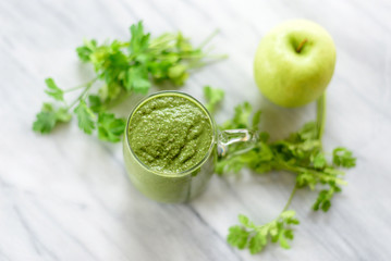 Green smoothie and fresh herbs on marble surface