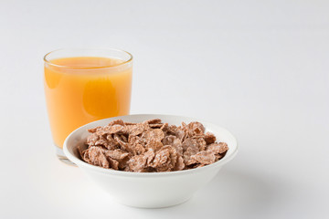 Bowl of multigrain natural flakes with glass of freshly squeezed orange juice on a white...