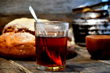 Bread, sugar, black tea in a glass, an old aluminum kettle on a wooden background.
