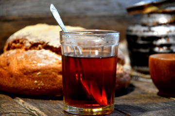 Bread, sugar, black tea in a glass, an old aluminum kettle on a wooden background.