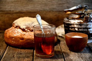 Bread, sugar, black tea in a glass, an old aluminum kettle on a wooden background.