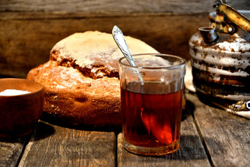 Bread, sugar, black tea in a glass, an old aluminum kettle on a wooden background.