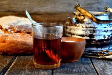 Bread, sugar, black tea in a glass, an old aluminum kettle on a wooden background.