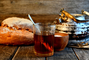 Bread, sugar, black tea in a glass, an old aluminum kettle on a wooden background.