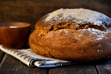 Loaf of bread, salt, napkin on a wooden background.
