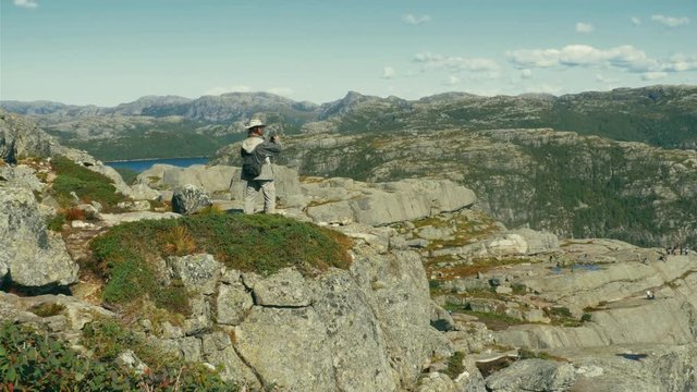 Male hiker with long hair and booney hat taking pictures of Pulpit rock, Preikestolen above Novergian Lysefjord in background, Scandinavian travel and mountain hiking concept