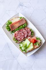 Fresh sandwiches with sausage, cheese, bacon, tomatoes, lettuce, cucumbers on a light background. Vertical orientation