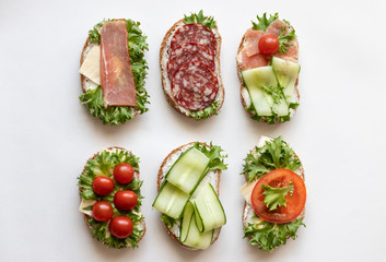 Fresh sandwiches with sausage, cheese, bacon, tomatoes, lettuce, cucumbers on a light background....