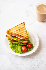 Sandwich with cheese, tomato, cucumber, sausage and salad on a light background. Coffee with milk. Vertical orientation