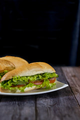 Two fresh underwater sandwiches with sausage, cheese, bacon, tomatoes, lettuce, cucumbers and onions on a dark wooden background