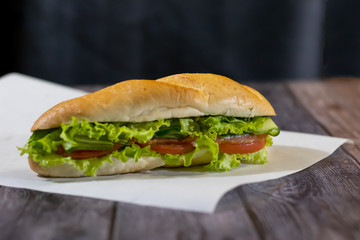 Two fresh underwater sandwiches with sausage, cheese, bacon, tomatoes, lettuce, cucumbers and onions on a dark wooden background