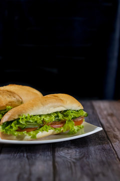 Two fresh underwater sandwiches with sausage, cheese, bacon, tomatoes, lettuce, cucumbers and onions on a dark wooden background