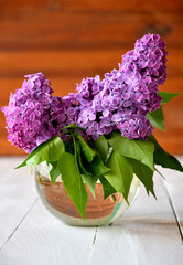 A bouquet of lilacs in a glass vase on a white table in the garden.