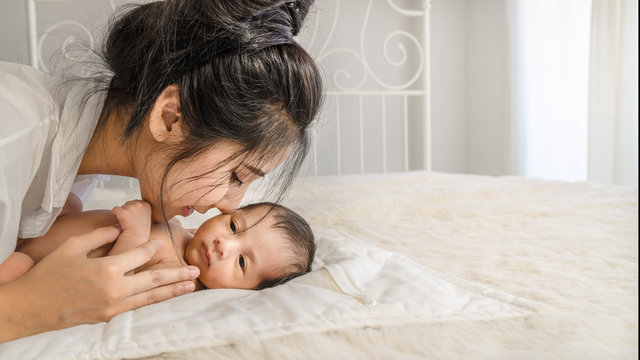 Asian mother holding and kissing her cute baby boy on bed