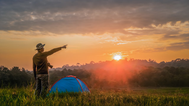 landscape scenery of tourist who pointing fingure have a camping with tent on grass field in natural park on sunrise
