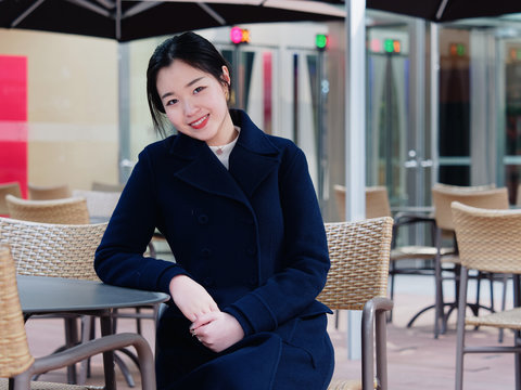 Portrait of a beautiful Chinese girl sitting and smiling in outdoor cafe, street photography of modern female.