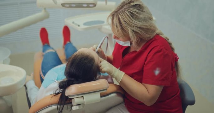 Dentist drills a tooth, removes the odontolith to the patient. Young girl at the reception at the dentist, oral hygiene. Modern dental clinic.