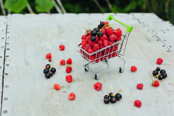 Mini shopping basket full of fresh red ripe raspberry and blackberry on vintage background