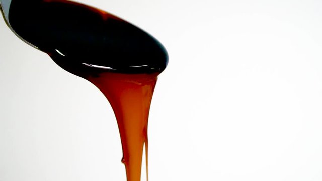 Molasses pours from spoon, slow motion, close up