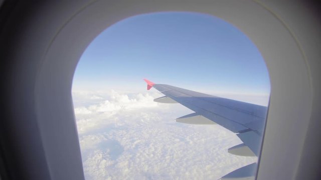 Airplane flight. Wing of an airplane flying above the clouds. View from the window of the plane. Aircraft. Traveling by air. 4K UHD video