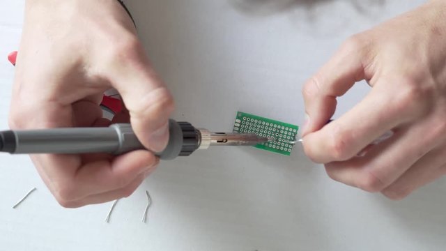 Top down close up footage of persons hands soldering self made electronic circuit at home. Window light from side. White Underground.
