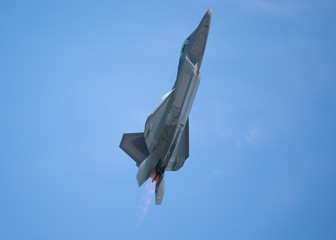 Fototapeta na wymiar F-22 Raptor in a high G climb in beautiful light , with condensation trails forming around the wings and afterburners on