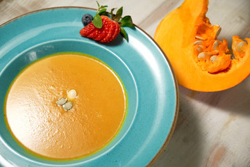 Pumpkin soup puree in a blue plate with pumpkin seeds. Light wooden background.