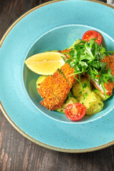 Breaded chicken with vegetables and herbs on a blue plate. Dark wooden background. Restaurant food.