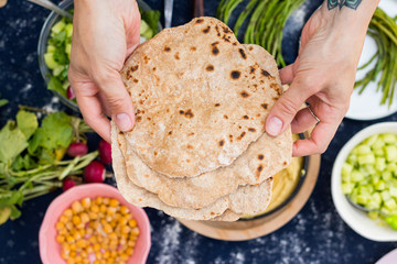 Woman hands holds hot homemade baked whole wheat flour Indian chapati crispy flat breads, pita, roti or paratha. Vegan food, vegetarian healthy food.