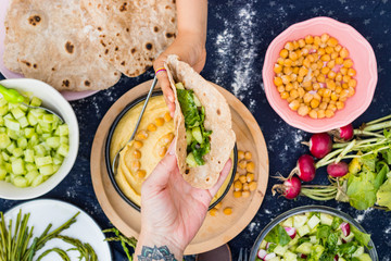 Adult woman hand gives to child or kid pita flat bread, chapati or roti with salad and creamy hummus for vegan lunch or vegetarian dinner. Family together having food.
