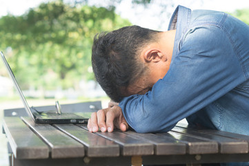 Fototapeta premium A man taking a break by sitting with falling his head down on the desk after using laptop in a public park