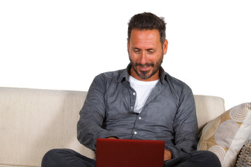 lifestyle portrait of young handsome and successful self employed man working at home using laptop computer sitting relaxed at living couch networking cheerful