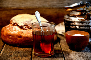 A glass of tea, bread, salt, an aluminum old kettle on a wooden table in the kitchen.