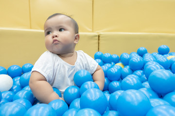 Happy Asian baby girl playing in a big dry pond full with blue plastic balls