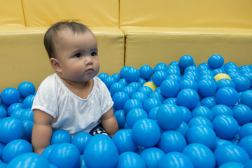 Fototapeta na wymiar Happy Asian baby girl playing in a big dry pond full with blue plastic balls