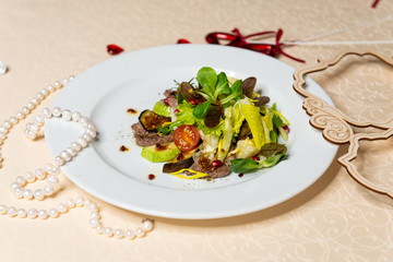 Salad from beef and fresh vegetables on a white plate in the interiors of the restaurant.