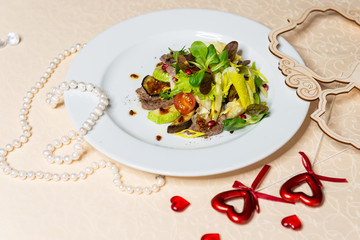 Salad from beef and fresh vegetables on a white plate in the interiors of the restaurant.