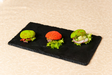 Three tartlets on a black plate in the interiors of the restaurant close-up. Cold snacks menu.