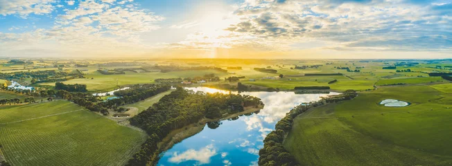 Fotobehang Ondergaande zon over schilderachtige graslanden en weiden op het Australische platteland met rivier die erdoorheen stroomt - luchtpanorama © Greg Brave