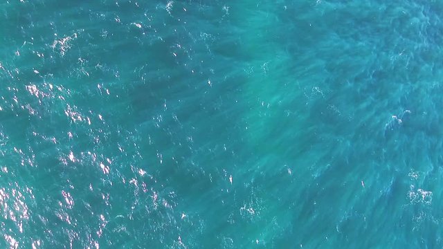 Aerial shot looking straight down on moving ocean waves with sun light shining through