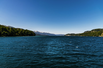 Fototapeta na wymiar Colorful nature scenic photo of transparent aquamarine blue water surface of a lake with forest and Andes mountains in Patagonia, Argentina