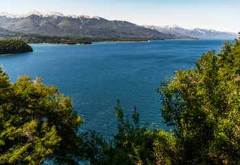 Fototapeta na wymiar Colorful nature scenic photo of transparent aquamarine blue water surface of a lake with forest and Andes mountains in Patagonia, Argentina