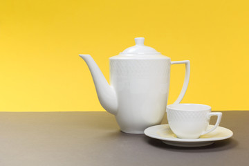 vintage white porcelain teapot and cup on gray board and yellow background