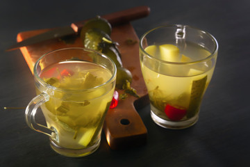 Two glass cups with cucumber pickle and pickled cucumbers with a knife on a wooden board. Close-up