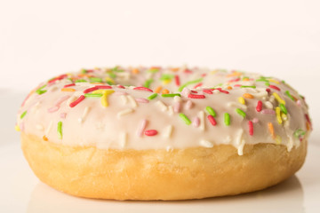 Fresh glazed donut with colorful sprinkles on a white plate.
