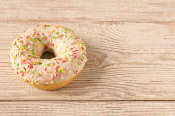 Fresh glazed donut with colorful sprinkles on a wooden table.